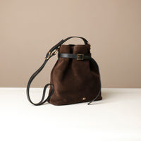 Brown suede leather bucket Danilos bag with black strap on a beige background