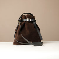 Brown leather handbag with black strap on a beige background