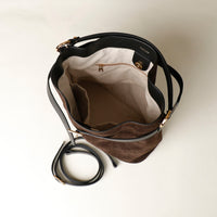 Upper view of a opened brown suede bucket Danilos bag with black strap on a light beige background