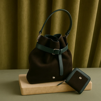 Black handbag with green accents and matching wallet on a wooden stand against a green curtain background