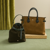 Two leather handbags, one brown and one black, on a green surface with a beige curtain in the background.