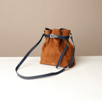 Brown suede bag with blue strap on a white surface and beige background