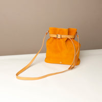 Yellow suede handbag with a strap on a white surface and beige background