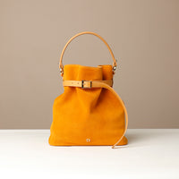 Mustard yellow suede leather bucket Danilos bag with gold accents on a beige background