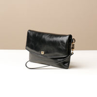 Side view of a glossy black leather Karelia Clutch Danilos with a visible hand strap over a white and beige background