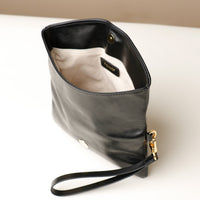 Upper view of an open glossy black leather Karelia Clutch Danilos with a visible hand strap over a white and beige background
