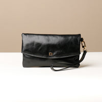 Front view of a glossy black leather Karelia Clutch Danilos with a visible hand strap over a white and beige background