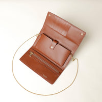 Opened Brown leather Danilos clutch with chain strap on a light beige background