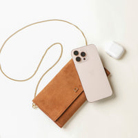 Brown suede Danilos clutch with gold chain, phone, and white case on a light background