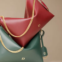 Two leather handbags, one red and one green, with gold chains and visible Danilos logo on a beige background.