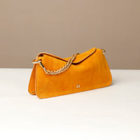 small Yellow suede leather danilos handbag with a gold chain on a white surface and beige background