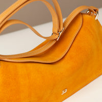 close-up of a small Yellow suede leather danilos handbag with a visible brand logo on a light background