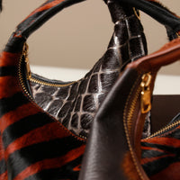 Close-up of a Danilos handbag with a black and grey texture on a surface and gold zipper.