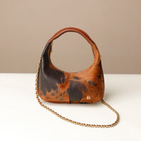 Brown and black patterned danilos  handbag with a gold chain on a white surface and beige background