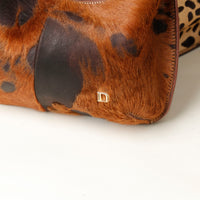 Close-up of a brown and black patterned handbag with a gold danilos logo on a white background