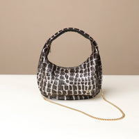 Black textured danilos  handbag with a gold chain on a beige background