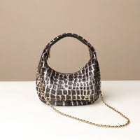 Black crocodile-patterned danilos  handbag with a gold chain on a beige background