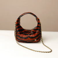 Zebra-striped hair on leather danilos  handbag with gold chain on a beige background