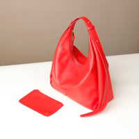 Red handbag and matching pouch on a white surface with a beige background