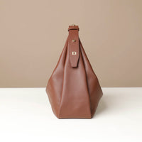 side view of a brown leather Mini Mia Minimale Danilos handbag with a strap on with the logo on it on a beige background