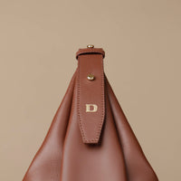close-up view of a brown leather Mini Mia Minimale Danilos handbag with a strap on and the logo on in over a beige background