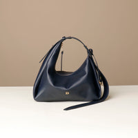 Front view of a marine blue leather Mini Mia Minimale Danilos handbag with a strap on a beige background