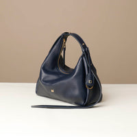 side view of a marine blue leather Mini Mia Minimale Danilos handbag with a strap on a beige background