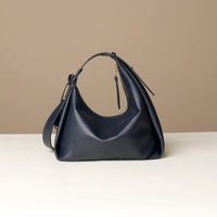 Back view of a marine blue leather Mini Mia Minimale Danilos handbag with a strap on a beige background