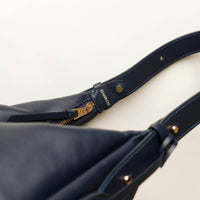 Close-up of a marine blue leather bag with a gold zipper and 'Danilos' branding on a white background