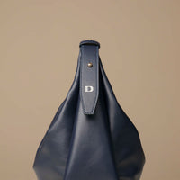 close-up view of a marine blue leather Mini Mia Minimale Danilos handbag with a logo on the strap on a beige background