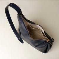upper view of an open marine blue leather Mini Mia Minimale Danilos handbag with a strap on a beige background