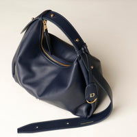 Mia Minimale Jr marine blue handbag with gold accents with logo Danilos on a tag on a light beige background