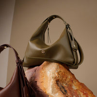close-up view of a green  leather Mini Mia Minimale Danilos handbag with a strap on over a rock in a beige background