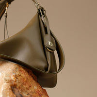 close-up view of a green  leather Mini Mia Minimale Danilos handbag with a strap on a beige background
