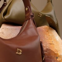 close-up view of two brown and green  leather Mini Mia Minimale Danilos handbag with a strap on a beige background
