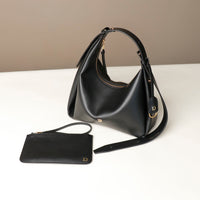 Black Danilos Mini Mia Minimale Jr handbag and matching wallet on a white surface with a beige background