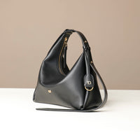 side view of a Black leather Mini Mia Minimale Danilos handbag with a strap on and gold accents in a beige background