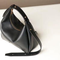 upper view of a Black leather Mini Mia Minimale Danilos handbag with a strap on and a gold zipper in a white background