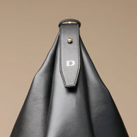 Close-up view of a Black leather Mini Mia Minimale Danilos handbag with a logo on the strap on a beige background