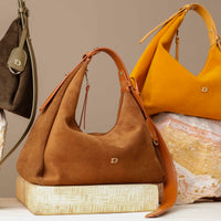 Brown suede handbag with a visible brand logo on a textured surface.