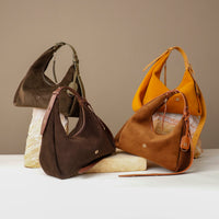 Four handbags in brown, yellow, and brown with strap on a neutral background