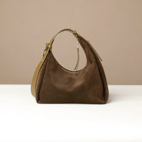 Brown leather handbag on a white surface with a beige background