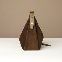 Brown suede handbag with a beige strap on a white surface and beige background
