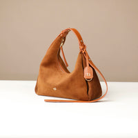 Brown handbag with a strap on a white surface and beige background