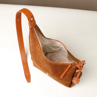Brown suede handbag with a strap on a white background