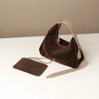 Brown handbag with beige strap on a white surface against a beige background