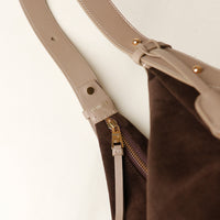 Close-up of a brown bag with a beige strap and gold zipper on a light background
