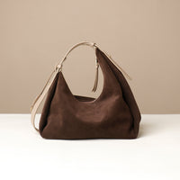 Brown leather handbag on a white surface with a beige background