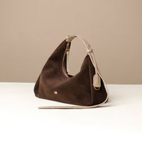 Brown handbag with beige strap on a white surface and beige background
