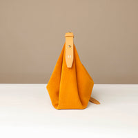 Yellow handbag with a strap on a white surface and beige background